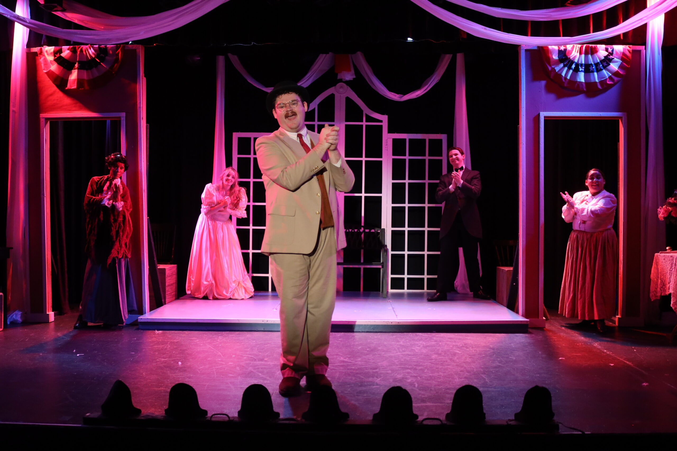 One man, center, receiving applause. Two individuals on each side flanking him in the background, dimly lit.
